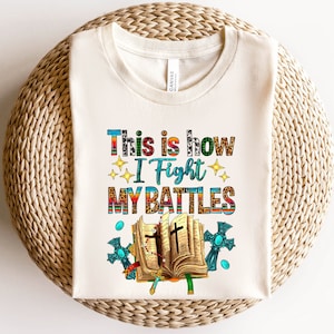 May include: A white t-shirt with the text "This is how I fight my battles" printed on it. The text is surrounded by a colorful design of a bible, crosses, and stars.