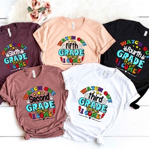 May include: Five t-shirts in different colors with the text "Watch Out [Grade] Here I Come" printed on them. The text is in a rainbow font with a peace sign and lightning bolt graphic. The grades are second, third, fourth, fifth, and sixth.