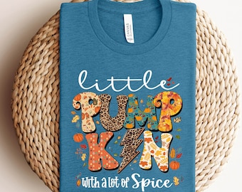 May include: A teal t-shirt with the words "little PUMPKIN with a lot of Spice" in a colorful, fall-themed design. The word "PUMPKIN" is decorated with leopard print, leaves, and pumpkins.