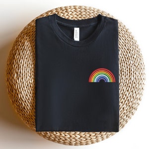 Op de afbeelding: Zwart T-shirt met een geborduurde regenboog op de voorkant. De regenboog is gemaakt van rood, oranje, geel, groen, blauw, indigo en violet garen.