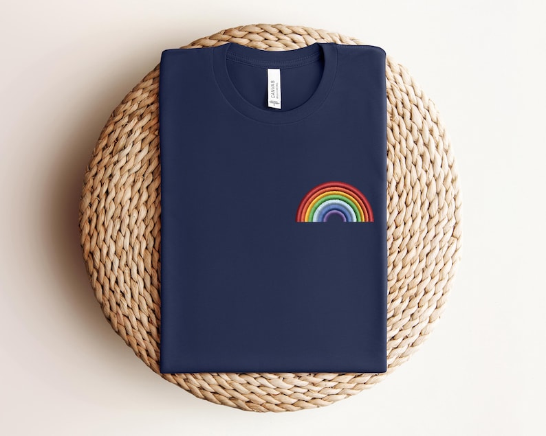 Op de afbeelding: Een marineblauw t-shirt met een geborduurde regenboog op de voorkant.