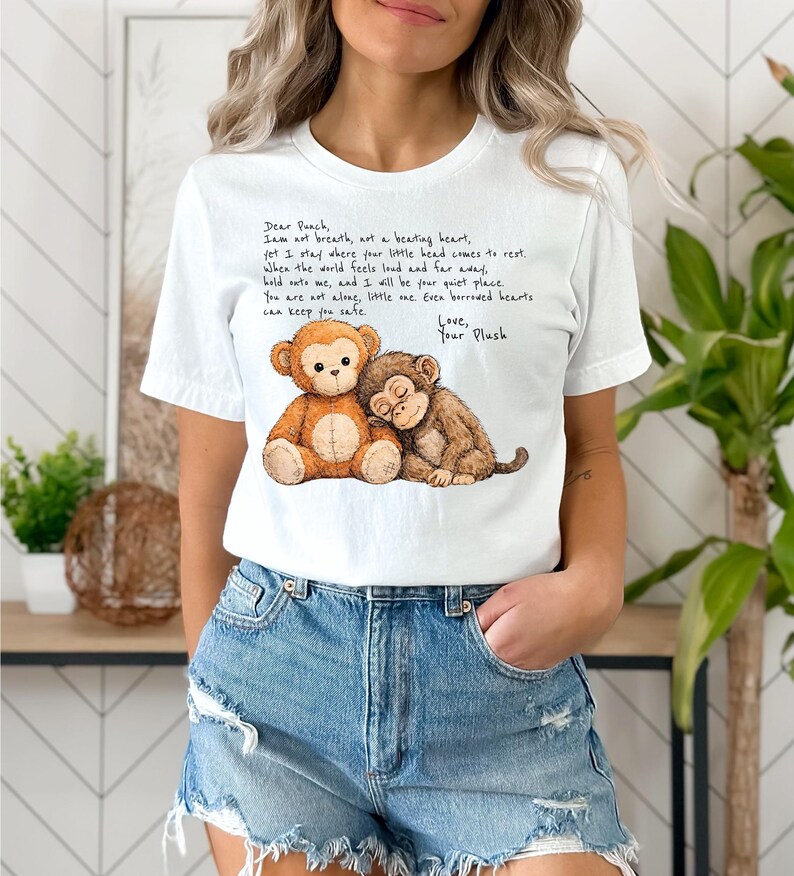 K&ouml;nnte beinhalten: Wei&szlig;es T-Shirt mit einer herzerw&auml;rmenden Illustration von zwei Stoffaffen. Einer ist hellbraun, der andere dunkelbraun, und sie umarmen sich. Das Shirt hat auch einen aufgedruckten Text.