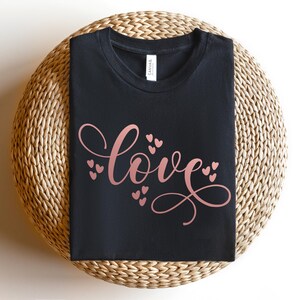 May include: A black t-shirt with the word "love" written in a cursive font in rose gold with small hearts surrounding the word.