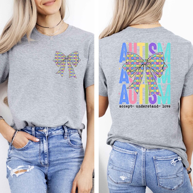 May include: A heather gray t-shirt featuring a colorful bow design with puzzle pieces. The front of the shirt has a small bow graphic, while the back displays the word "AUTISM" and the phrase "accept- understand- love".