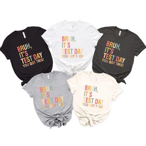 May include: Five t-shirts in different colors with the text "Bruh, it's test day you got this!" in colorful letters. The shirts are all short-sleeved and have a crew neck.