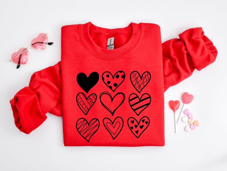 May include: Red sweatshirt with a graphic of nine black hearts with different patterns on the front. The hearts are arranged in a grid pattern.
