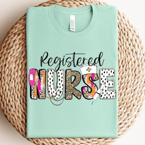 May include: A light green t-shirt with the words "Registered Nurse" in a black script font. The word "NURSE" is designed with a bandage, leopard print, gold glitter, and a nurse's hat and syringe.