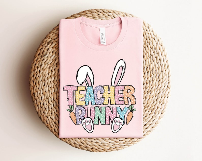 May include: Pink t-shirt with a graphic of a bunny with the text "Teacher Bunny" in rainbow colors with white polka dots.