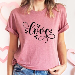 May include: A pink t-shirt with the word "love" written in black cursive script with small hearts surrounding the word.