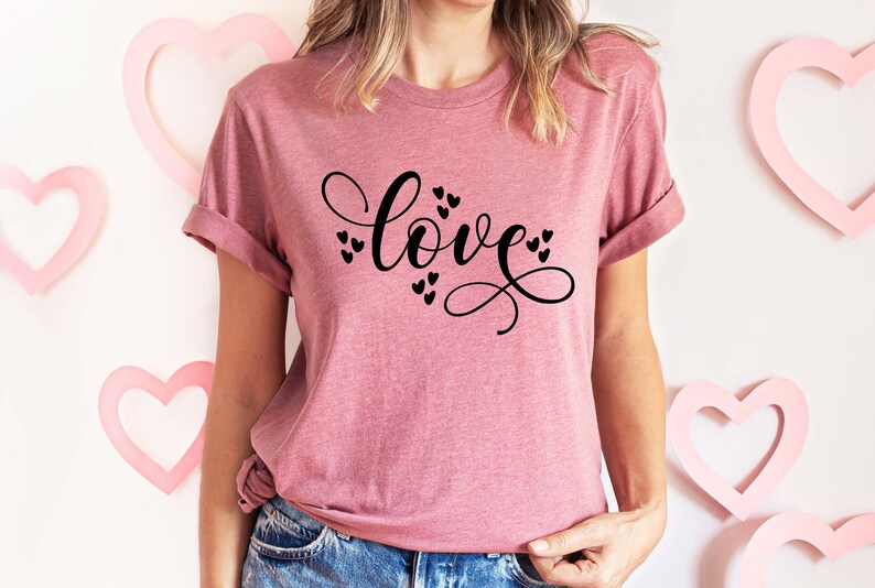 May include: A pink t-shirt with the word "love" written in black cursive script with small hearts surrounding the word.