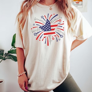 May include: A white t-shirt with a red, white, and blue star design. The star is surrounded by fireworks and the words "fireworks", "4th of July", "family", "freedom", and "icecream".