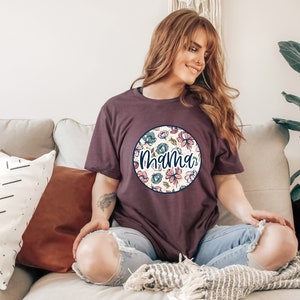Może przedstawiać: Kobieta w bordowym t-shircie z białym kołem ozdobionym kwiatowym wzorem i napisem "Mama" w granatowym kolorze.
