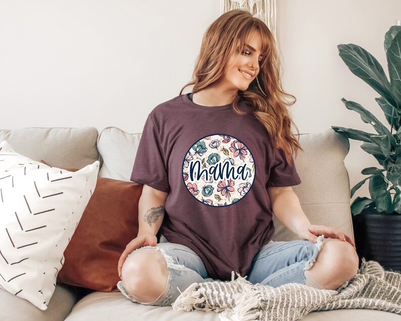 Może przedstawiać: Kobieta w bordowym t-shircie z białym kołem ozdobionym kwiatowym wzorem i napisem "Mama" w granatowym kolorze.
