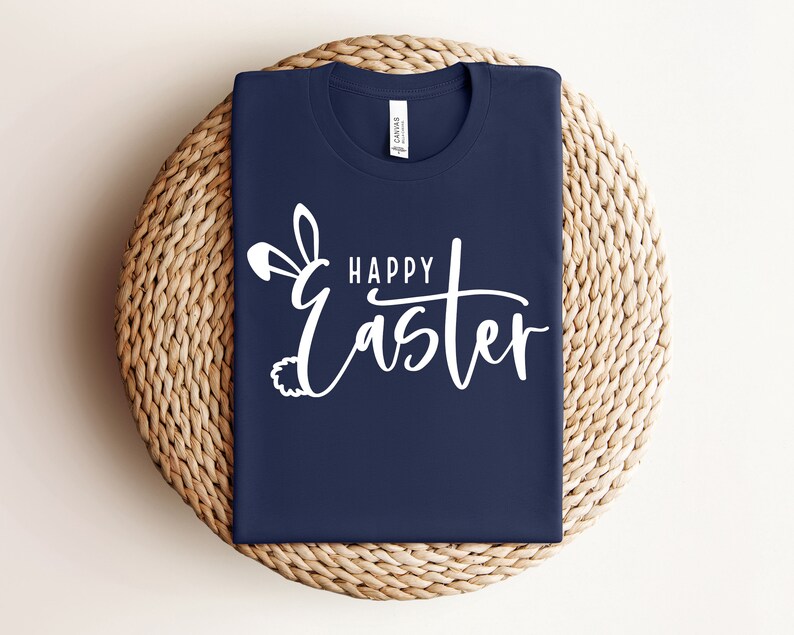 Puede incluir: Una camiseta azul marino con un dise&ntilde;o de orejas de conejo blancas y el texto "Happy Easter" en escritura blanca.