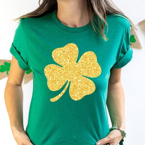 May include: A green t-shirt with a gold glitter four-leaf clover design.