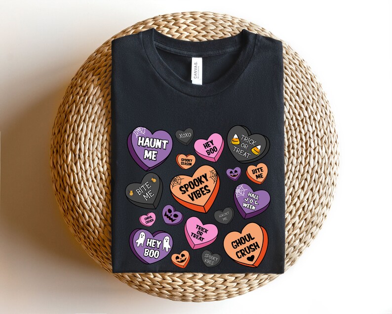 Puede incluir: Camiseta negra con un dise&ntilde;o de tem&aacute;tica de Halloween con corazones de caramelo con frases como "Haunt Me", "Spooky Vibes", "Ghoul Crush" y "Trick or Treat".