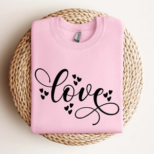 May include: Pink sweatshirt with the word "love" written in black cursive script with small hearts surrounding the word.