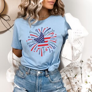 May include: A light blue t-shirt with a red, white, and blue star design. The star is surrounded by fireworks and the words "fireworks", "4th of July", "family", "freedom", and "ice cream".