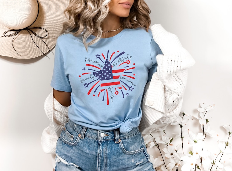 May include: A light blue t-shirt with a red, white, and blue star design. The star is surrounded by fireworks and the words "fireworks", "4th of July", "family", "freedom", and "ice cream".