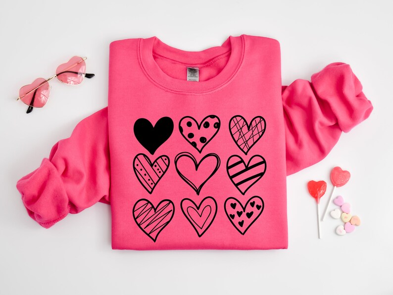 May include: A pink sweatshirt featuring a black design of nine different hearts. The hearts are all different shapes and sizes and have various patterns.