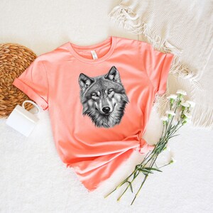 以下が含まれることがあります： 黒と白のオオカミのグラフィックプリントが施されたコーラルピンクのTシャツです