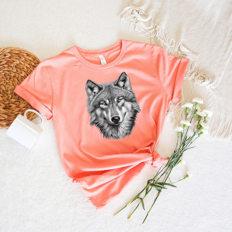 以下が含まれることがあります： 黒と白のオオカミのグラフィックプリントが施されたコーラルピンクのTシャツです