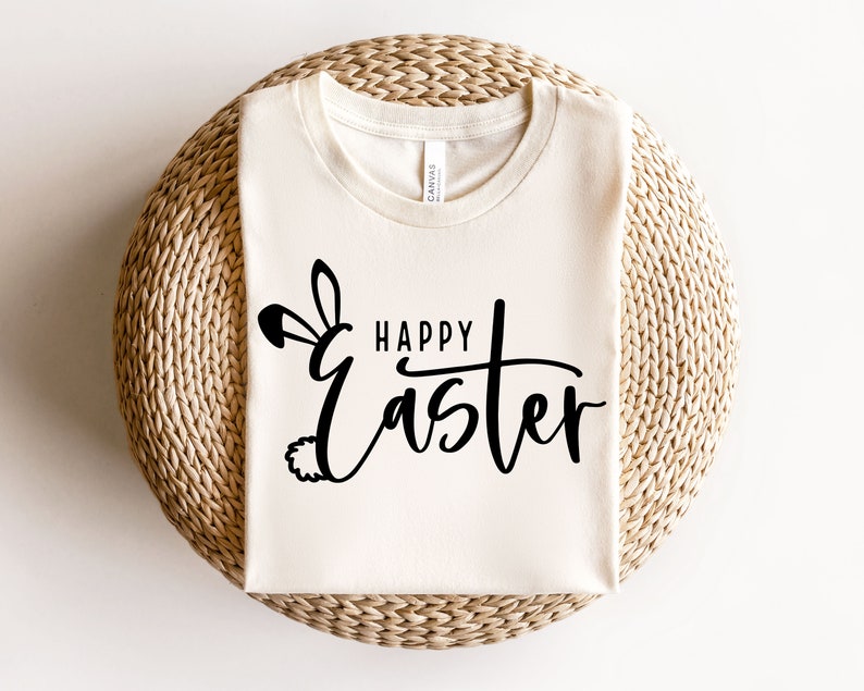 Puede incluir: Una camiseta blanca con un dise&ntilde;o de orejas de conejo negras y el texto "Happy Easter" en una fuente cursiva.
