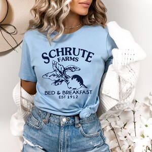 May include: A light blue t-shirt with a navy blue graphic of a beet and the text "Schrute Farms Bed & Breakfast Est 1912".