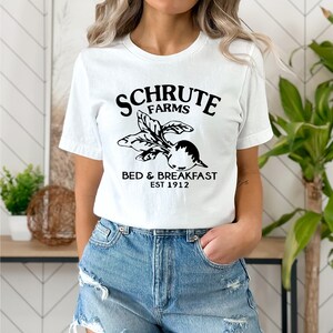 May include: White t-shirt with black text that reads "Schrute Farms Bed & Breakfast Est 1912" and a black graphic of a beet.