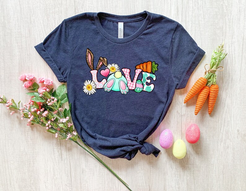 May include: A navy blue t-shirt with a graphic of a bunny rabbit and the word "LOVE" in colorful letters. The letters are decorated with flowers, carrots, and Easter eggs.