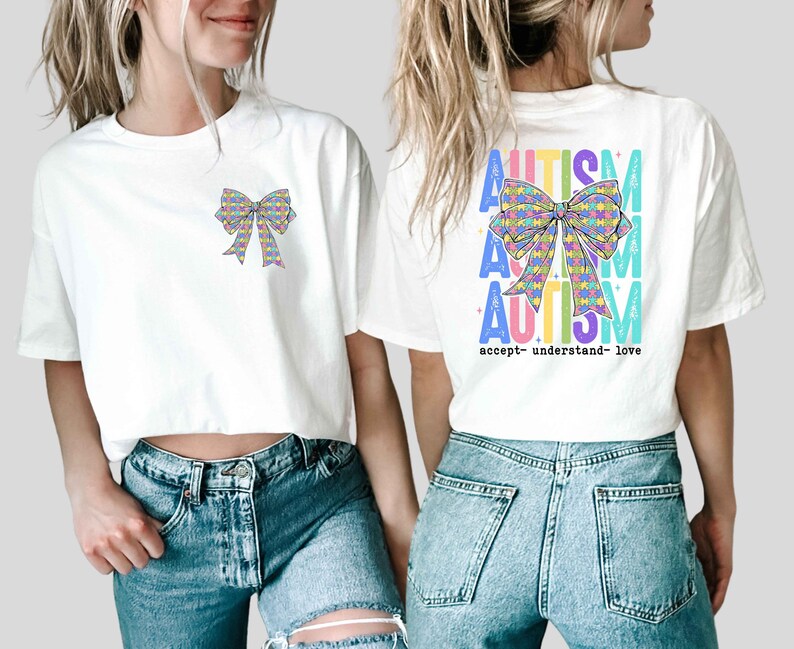 May include: White t-shirts with a colorful bow design. One shirt has the bow on the front, the other on the back with the word "AUTISM" in multiple colors and the words "accept- understand- love".