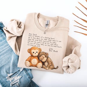 K&ouml;nnte beinhalten: Beiges Sweatshirt mit einem Aufdruck von zwei Cartoon-Affen und handgeschriebenem Text. Der Text lautet "Dear Peach, I am not breath, not a beating heart..." Das Sweatshirt wird mit einer blauen Jeans gezeigt.