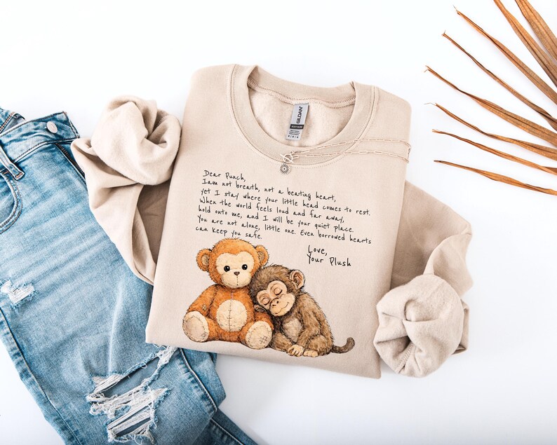 K&ouml;nnte beinhalten: Beiges Sweatshirt mit einem Aufdruck von zwei Cartoon-Affen und handgeschriebenem Text. Der Text lautet "Dear Peach, I am not breath, not a beating heart..." Das Sweatshirt wird mit einer blauen Jeans gezeigt.