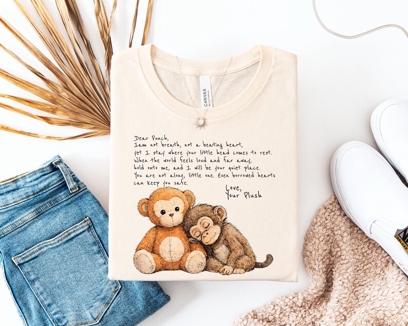 K&ouml;nnte beinhalten: Cremefarbenes T-Shirt mit einer Aquarellillustration von zwei Pl&uuml;schaffen. Einer sitzt, der andere schl&auml;ft. Das Shirt hat handgeschriebenen Text, der lautet: "Dear Punch, I am not breath..." und endet mit "Love, Your Plush."