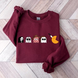Pode incluir: Camisola de cor bord&ocirc; com um gr&aacute;fico de personagens de filmes de terror como fantasmas Pac-Man. Os personagens incluem Ghostface, Jason Voorhees, Freddy Krueger e Michael Myers. O fantasma Pac-Man est&aacute; sendo perseguido por uma faca.