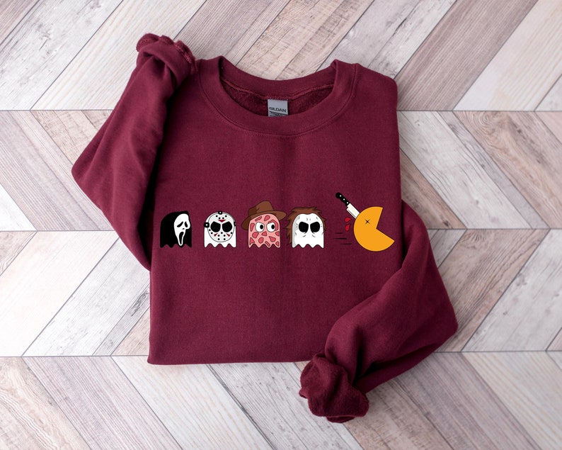 Pode incluir: Camisola de cor bord&ocirc; com um gr&aacute;fico de personagens de filmes de terror como fantasmas Pac-Man. Os personagens incluem Ghostface, Jason Voorhees, Freddy Krueger e Michael Myers. O fantasma Pac-Man est&aacute; sendo perseguido por uma faca.