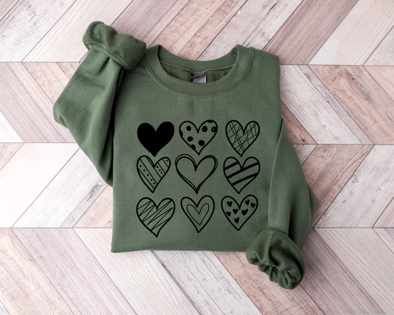 May include: A green sweatshirt with a black graphic of various hearts with different patterns.