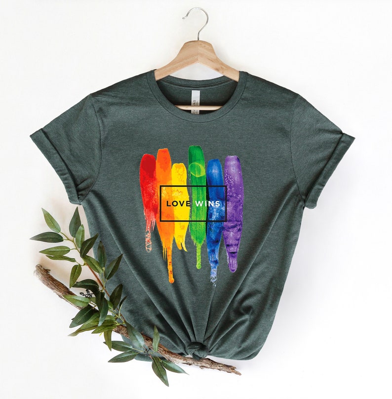 May include: A dark green t-shirt with a rainbow paint splatter design and the text "LOVE WINS" in a black box.