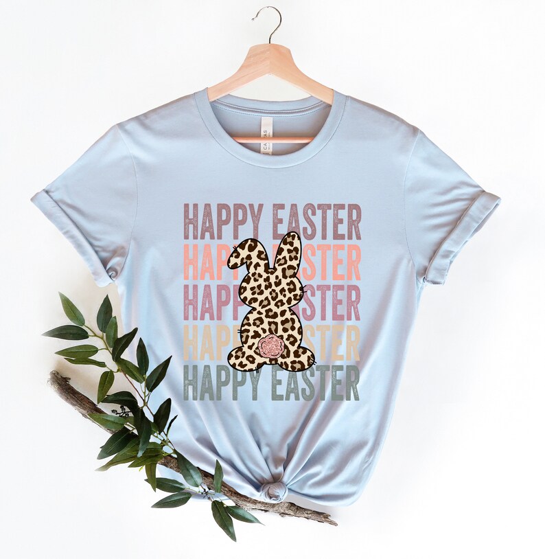 May include: Light blue t-shirt with the text "Happy Easter" repeated in a stacked design with a leopard print bunny in the center. The text is in a vintage style font with pink, orange, and yellow colors.