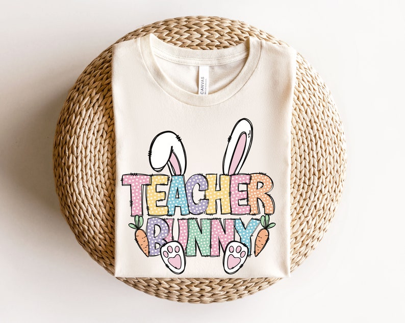 May include: A white t-shirt with a colorful graphic that says "Teacher Bunny" with bunny ears, paw prints, and carrots.