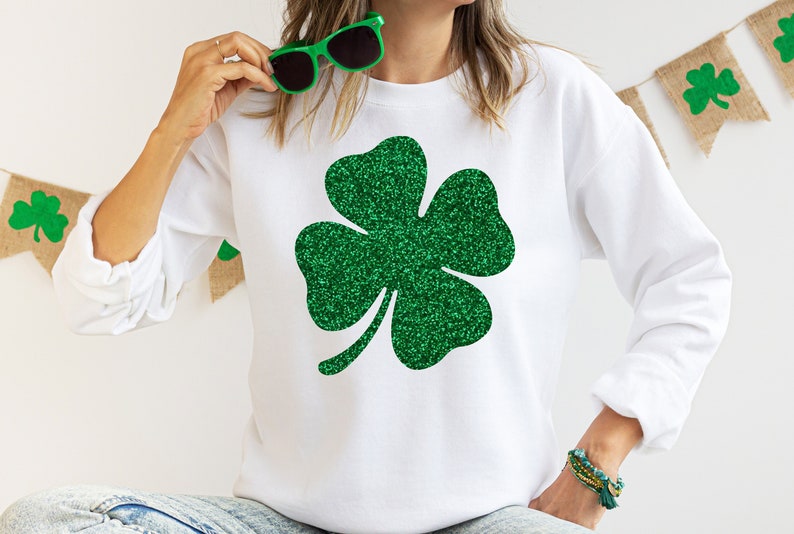 May include: White sweatshirt with a green glitter shamrock design.