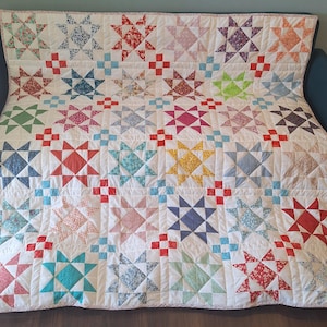May include: A patchwork quilt with a star design in a variety of colours, including red, blue, green, and yellow, on a white background. The quilt is made of fabric squares and is suitable for bedding or decorative purposes.