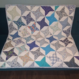 May include: A rectangular patchwork quilt featuring a repeating star pattern. The quilt is constructed from various fabric squares in shades of blue, white, and teal, with diverse floral, geometric, and polka dot prints throughout the design.