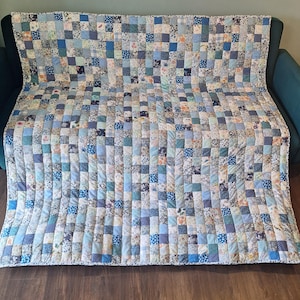 May include: A patchwork quilt in shades of blue, white, and cream, draped over a teal sofa. The quilt is made of numerous small squares with floral and geometric patterns. The quilt's dimensions are approximately 178 cm by 203 cm.
