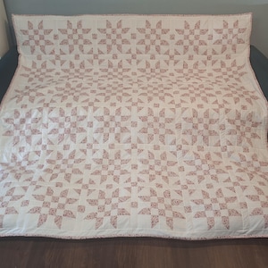 May include: A large rectangular quilt featuring a repeating star pattern. The design consists of white fabric blocks alternating with blocks patterned in a small-scale red floral print. The quilt has a thin red floral border along the edges.