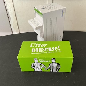 May include: A green box of the game "Utter Nonsense!" with two illustrated men on the front. A white box of cards is behind it. The game box has the text "The Hilarious Game of Voices and Accents."
