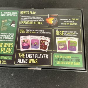 Może przedstawiać: Czarne pudełko do gry Exploding Kittens, z ilustracjami i tekstem. Pudełko zawiera instrukcje, przykłady kart i frazę &bdquo;Ostatni gracz, kt&oacute;ry przeżyje, wygrywa&rdquo;. Gra jest rodzinna i może być rozgrywana przez maksymalnie 5 graczy.