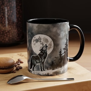 May include: A black ceramic coffee mug with a wolf howling at the moon design. The moon is full and white with a gray watercolor background. The wolf is black and gray and is standing on a grassy hill. The mug has a black handle.
