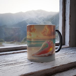 Peut inclure: Une tasse en céramique blanche avec une anse noire présente un coquillage coloré sur une plage au coucher du soleil. La tasse est remplie d'une boisson fumante.