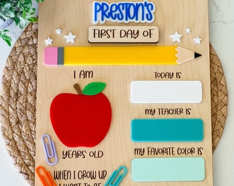 Könnte beinhalten: Ein hölzernes Schild für den ersten Schultag mit dem Namen Preston in Blau, einem gelben Stift, einem roten Apfel und bunten Acryl-Akzenten. Das Brett enthält leere Felder zum Ausfüllen von Details wie Alter, Lehrer, Lieblingsfarbe und Berufswunsch.